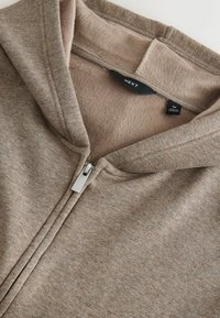 Hættetrøje med lynlås, lavet af blødt brunt stof med en glat tekstur, udstyret med en sølvfarvet lynlås og inderfor af fleece.