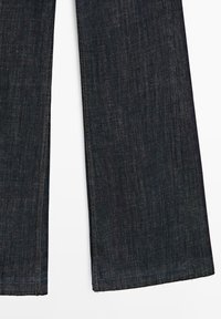 Mörkblå denimbyxor med vida ben, en slät textur och fransiga kanter. Har diskreta sömmar längs med sömmarna.