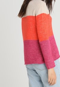 Mehrfarbiger Strickpullover mit horizontalen Streifen in Beige, Orange und Pink. Weiche Textur mit lockerer Passform und langen Ärmeln.
