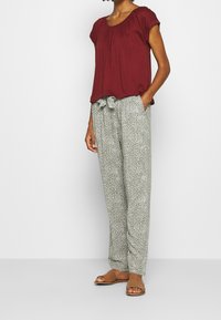 Burgunderfärgad kortärmad blus med rynkad halsringning, matchad med ljusgrönmönstrade byxor som har dragsko i midjan och sidofickor.