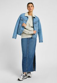 Chaqueta de mezclilla con cuello de borrego, sudadera gris, falda de mezclilla azul hasta la rodilla con abertura, zapatillas en blanco y negro. Atuendo casual.