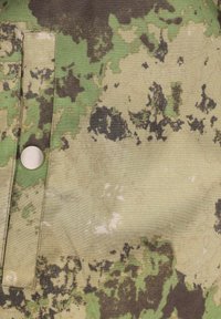 Kamouflage-tyg i gröna och svarta nyanser, med en texturerad yta, en silverfärgad tryckknapp och en fickdetalj med patch.