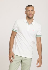 Polo shirt blanc avec des accents de col et de poignets à rayures vertes ; manches courtes ; détail de logo rouge sur la poitrine ; tissu en coton, design ajusté.