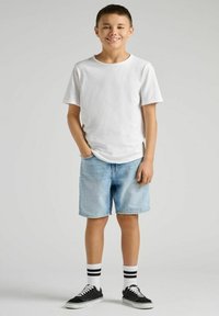 Biała koszulka typu crew-neck, jasnoniebieskie szorty dżinsowe, czarne trampki, białe skarpetki w czarne paski. Luźny krój, prosty design oraz klasyczne kolory.