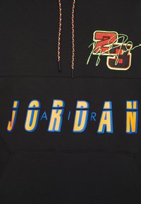 Sudadera negra con cordones coloridos, gran texto "JORDAN" en amarillo y azul, y el "23" en rojo con bordado de firma en verde.