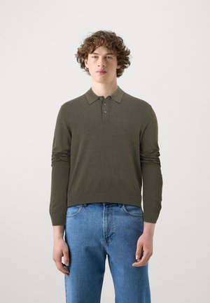 Polo a maniche lunghe verde scuro in maglia tessuta, con colletto e chiusura a tre bottoni, abbinato a jeans azzurri chiari.