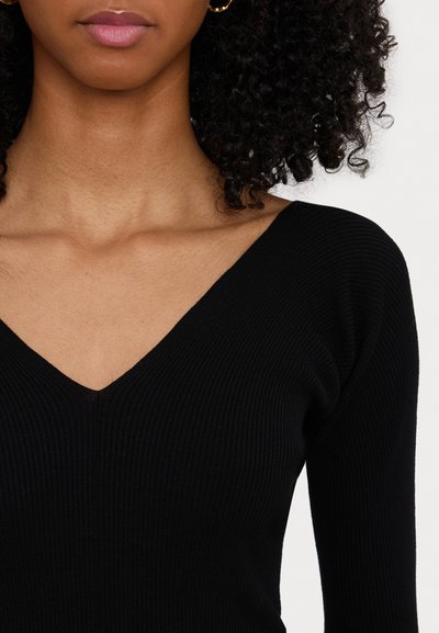 Un haut noir à poignets longs en maille côtelée, présentant un décolleté en V et une silhouette ajustée. La texture est lisse et le tissu semble extensible.