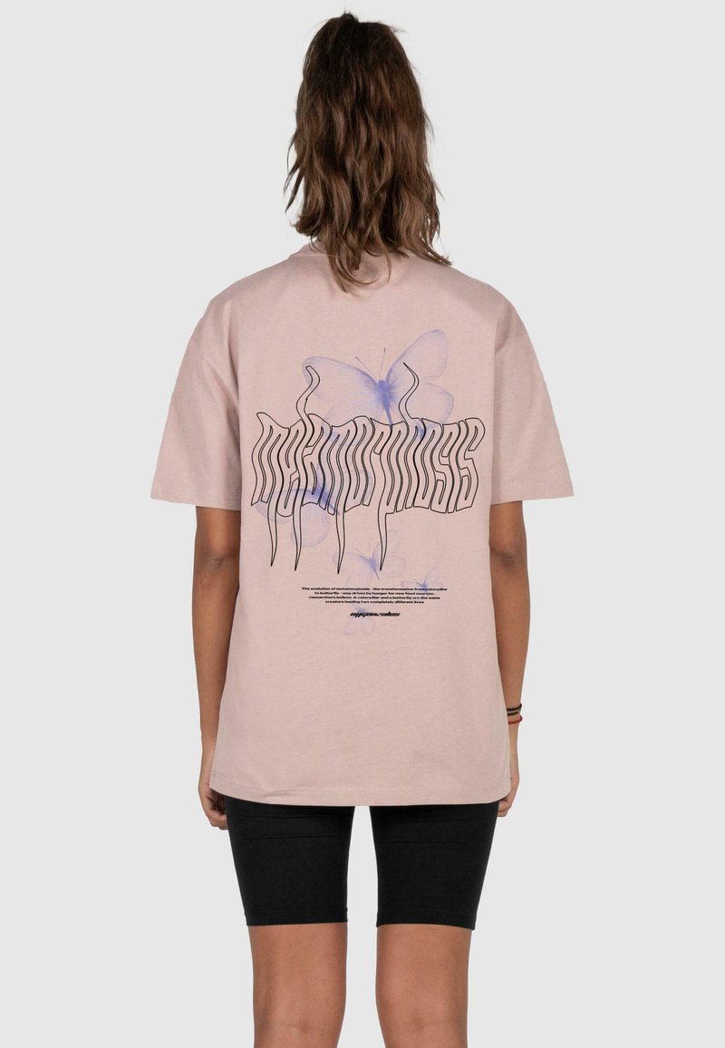 Lys rosa bomulds t-shirt med et grafisk design af en blå sommerfugl og stiliseret tekst på ryggen. Korte ærmer og afslappet pasform.