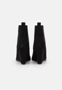 Bottines à talon en suède noir avec une texture lisse, un dos rétréci, des accents élastiques sur les côtés et un léger talon.