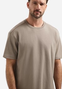 Khaki t-shirt met korte mouwen, gemaakt van een gladde katoen. Heeft een ronde halslijn en een ontspannen pasvorm, met zichtbare stiksels langs de randen.