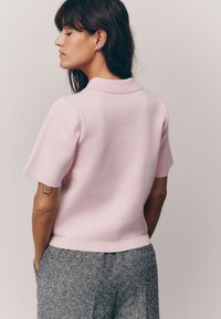 Korte mouw roze gebreide polo met kraag, met een getailleerd ontwerp en geribbelde zoom, gedragen met grijze gemusterde broek.