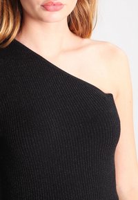 Top nero a spalla unica realizzato in tessuto a coste con un leggero lucido. Caratterizzato da un design aderente e una texture liscia. Nessun motivo visibile o hardware.
