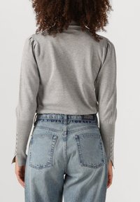 Graues Langarmoberteil mit gepufften Schultern und geknöpften Manschetten, kombiniert mit blauen hochsitztenden Jeans mit Gesäßtaschen und gesticktem Bund.