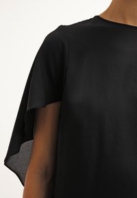 Sort top med rund halsudskæring og korte, draperede ærmer. Stoffet ser glat ud med en subtil glans og ingen synlige mønstre.