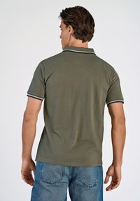 Olivengroen poloshirt met een gestructureerde stof, voorzien van een geribde kraag en gestreepte accenten in marineblauw en wit. Draagt bij blauwe spijkerbroeken.