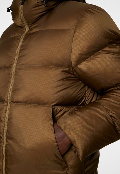 Brun puffjacka tillverkad av slät, quiltad material med hög krage, frontdragkedja och sidofickor. Har ett subtilt texturmönster.