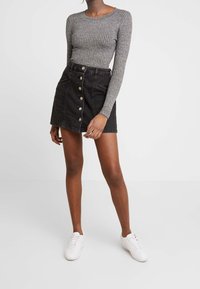 Haut gris à manches longues côtelé associé à une jupe trapèze en jean noir avec des boutons argentés et des poches latérales, porté avec des baskets blanches.