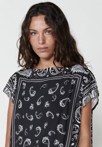 Un haut noir avec un motif cachemire blanc, doté d'un col bateau et de manches courtes. Fabriqué à partir d'un matériau léger et fluide.