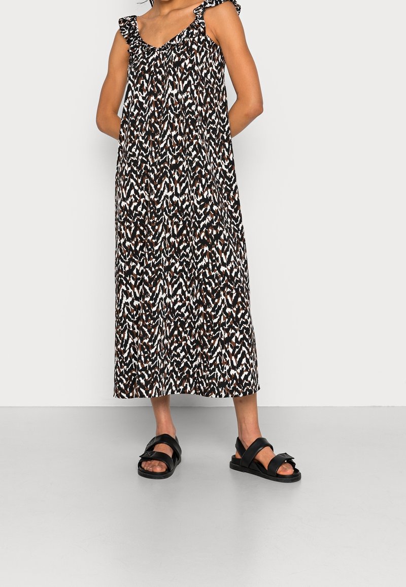 Robe longue à motif chevron noir, blanc et marron avec bretelles à volants. Associée à des sandales plates noires, avec larges brides et boucle.