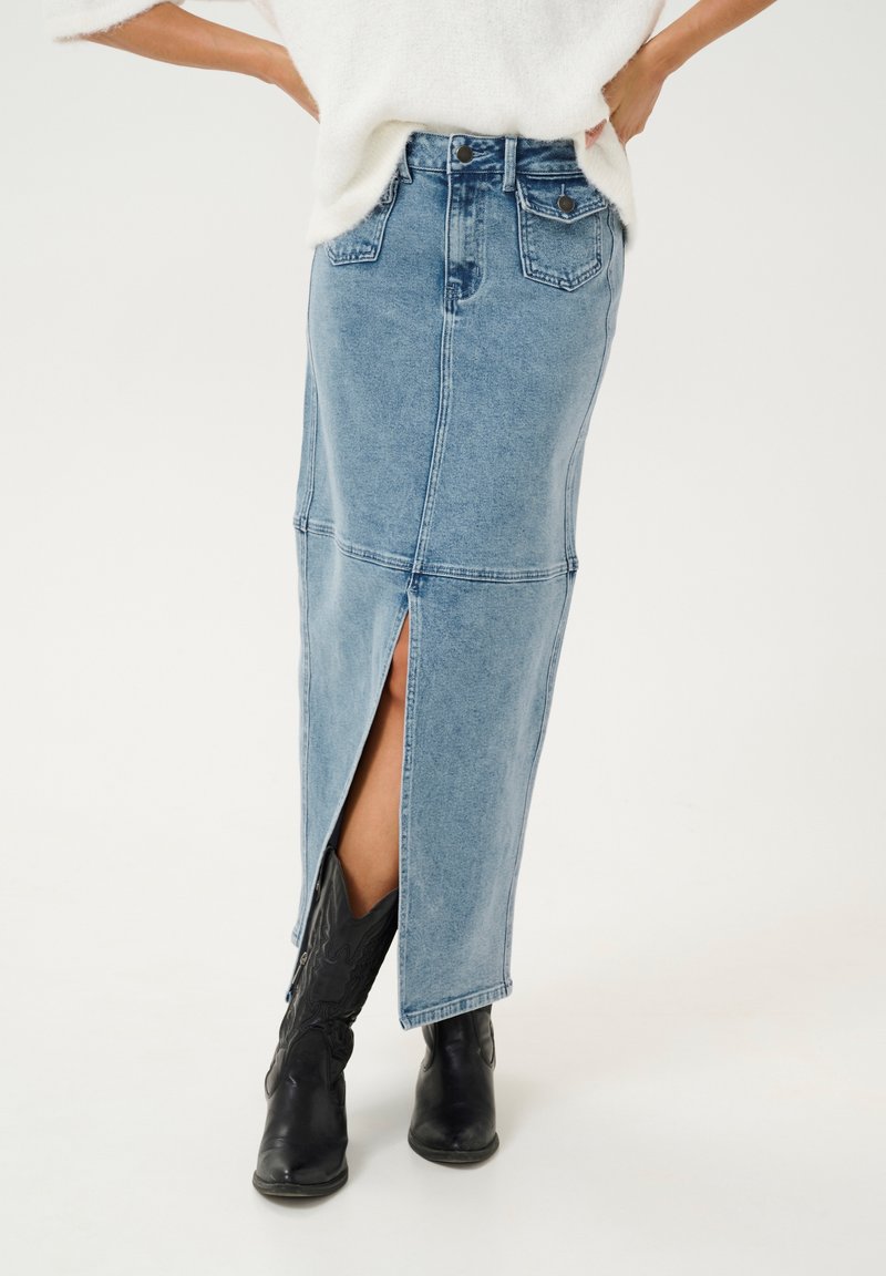 Jeans-Maxikleid mit einem vorderen Schlitz, hellblaue Farbe, klassisches Fünf-Taschen-Design und kontrastierende Nähte. Getragen mit schwarzen Cowboystiefeln.