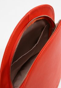 Czerwona skórzana torba na zamek, otwarta, aby pokazać pustą beżową tkaninę wewnętrzną z przegrodą szytą.