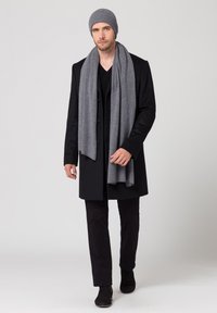 Cappotto nero, sciarpa grigia, berretto di lana grigio, camicia nera e pantaloni neri. Tessuti morbidi e design su misura per il freddo.