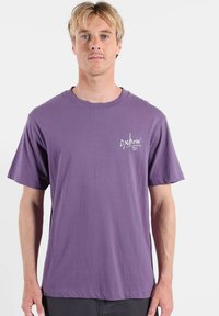 T-shirt en coton violet à manches courtes, col rond, avec un petit logo blanc sur la poitrine gauche. Texture lisse et coupe décontractée.