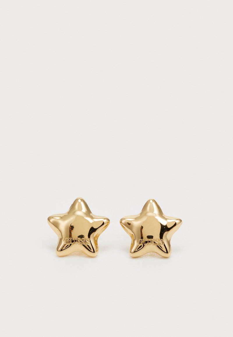 Brincos em forma de estrela dourada com um acabamento brilhante. Nome da marca "GUESS" gravado de um lado, destacando os detalhes do design e da textura.