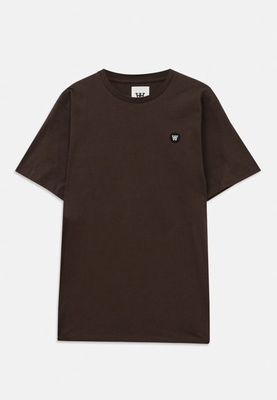 T-shirt marron foncé à manches courtes avec un col rond et un petit patch logo noir et blanc sur le haut à gauche de la poitrine.
