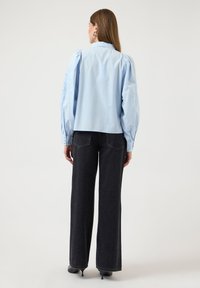 Ανοιχτό μπλε μπλούζα με φουσκωτά μανίκια, κεντητικές λεπτομέρειες στο αριστερό μανίκι και μαύρο τζιν ψηλόμεσο με φαρδιά μπατζάκια.