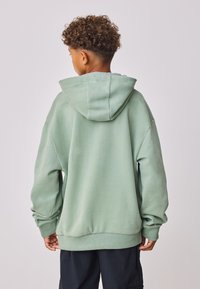 Menta zöld kapucnis pulóver tágas kapucnival, laza szabással, leengedett vállakkal és bordázott mandzsettákkal. Puha, texturált anyag minták nélkül.