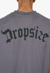 Grauem Baumwoll-T-Shirt mit großen schwarzen gotischen Buchstaben "Dropsize" auf dem Rücken gedruckt. Kurze Ärmel und runder Ausschnitt.