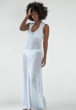 Jasnoniebieska dzianinowa sukienka z głębokim dekoltem w kształcie litery V, o długiej, swobodnej sylwetce oraz teksturowanym wzorze. Materiał jest półprzezroczysty, podkreślając kształt ciała.