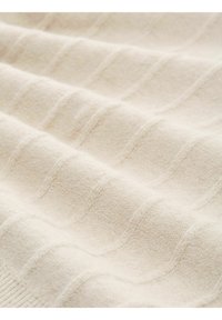 Beige strukturiertes Gewebe mit einem Wellenmuster. Das Material wirkt weich und gewebt und zeigt subtile Variationen in der Dicke an der Oberfläche.