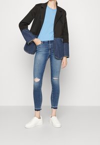 Blazer negro con detalles en denim, camiseta de color azul claro, jeans ajustados desgastados y zapatillas blancas. Diseño sencillo y contemporáneo, apariencia casual.