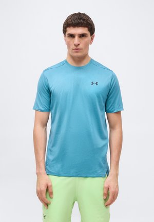 Bărbat purtând un tricou sport cu mâneci scurte Under Armour albastru deschis și pantaloni scurți Under Armour verde deschis, stând în fața unui fundal simplu, luminos.