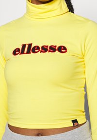 Gelbes Rollkragenoberteil mit langen Ärmeln, ausgestattet mit rotem "ellesse"-Logo. Glatter, dehnbarer Stoff mit figurbetonendem Design und Logostickerei am Saum.