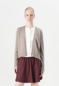Bruine wollen cardigan met geribbelde manchetten, open voorkant, gecombineerd met een witte button-up top en een kastanjebruine rok met een zak. Eenvoudig, textuur ontwerp.