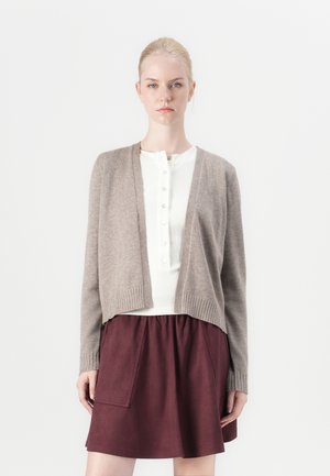 Brun ullcardigan med ribbade muddar, öppen framsida, ihop med en vit skjortblus och en vinröd kjol med ficka. Enkel, strukturerad design.