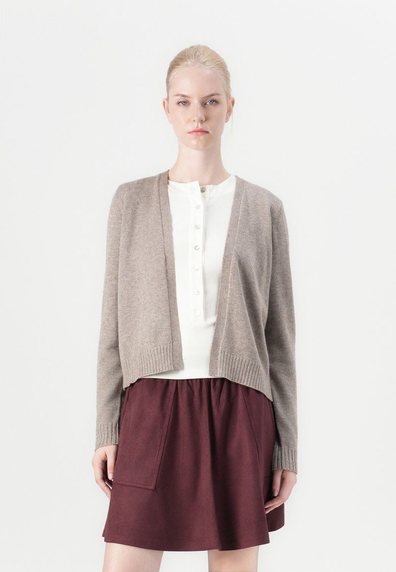 Bruine wollen cardigan met geribbelde manchetten, open voorkant, gecombineerd met een witte button-up top en een kastanjebruine rok met een zak. Eenvoudig, textuur ontwerp.