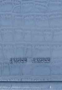 Sinine kunstnahk koos krokodillinahkse tekstuuriga, millel on reljeefne "SAMSOE SAMSOE" brändinimi. Sile pind ja peen läige.