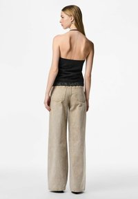 Melns strapless tops ar teksturētu audumu un mežģīņu apakšmalu, kopā ar augsta vidukļa, vaļēja piegriezuma bēša krāsas džinsiem ar viegli izbalinātu apdari.