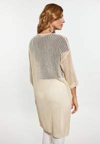 Cardigan lungo beige a maglia con tessuto aperto, maniche a tre quarti e vestibilità comoda. Caratterizzato da una texture morbida e un design con schiena aperta.