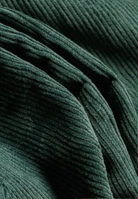 Σκούρο πράσινο πανί καλλιεργητή που δείχνει κάθετη ραβδωτή υφή, με μαλακή, ελαφρώς γούνινη επιφάνεια και επικάλυπτες πτυχές.