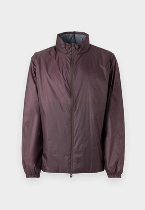 Giacca leggera color bordeaux con colletto alto, zip a tutta lunghezza, polsini elasticizzati e una texture liscia e leggermente lucida.