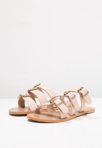 Infradito nude con molteplici cinturini morbidi, realizzati in pelle e con fibbie in tono oro, suole piatte e design minimalista.