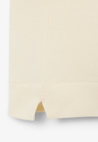 Close-up van crèmekleurige, gestructureerde stof met een kleine zijschuif aan de zoom, met gedetailleerde stiksels.