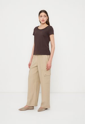 Woman wearing dark brown short-sleeve top, beige wide-leg cargo pants, and beige flats, standing against a plain white background.