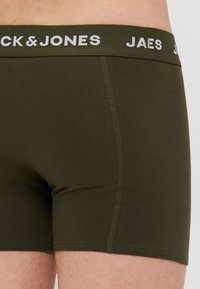 Olivgrüne Boxershorts aus weichem Material mit einem weißen Markengummibund. Nahtdetails an den Seiten verleihen Struktur.