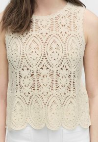 Ivory lace crop top, joka on koristeltu monimutkaisilla kukka- ja lehtikuvioilla. Hieman kaareva helma lisää tekstuuria ja yksityiskohtia kevyelle vaatteelle.